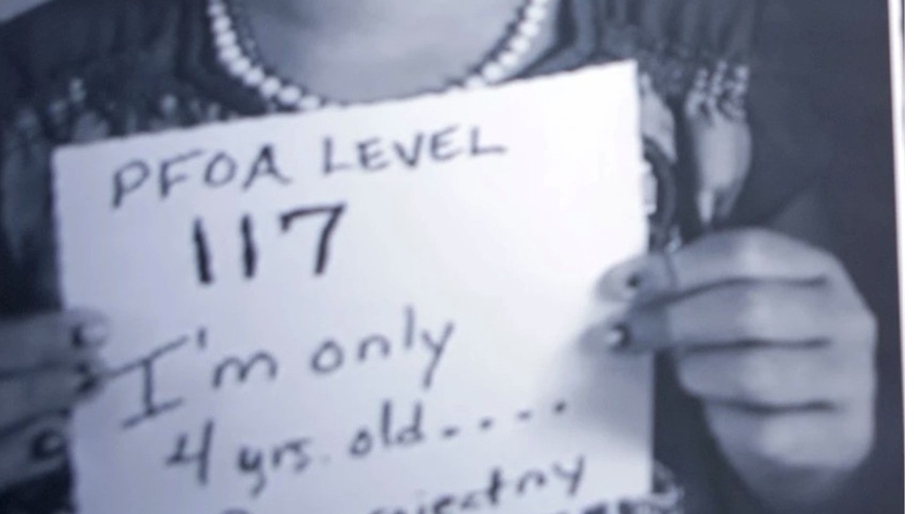 Kind hält ein Schild mit seinen PFOA-Werten