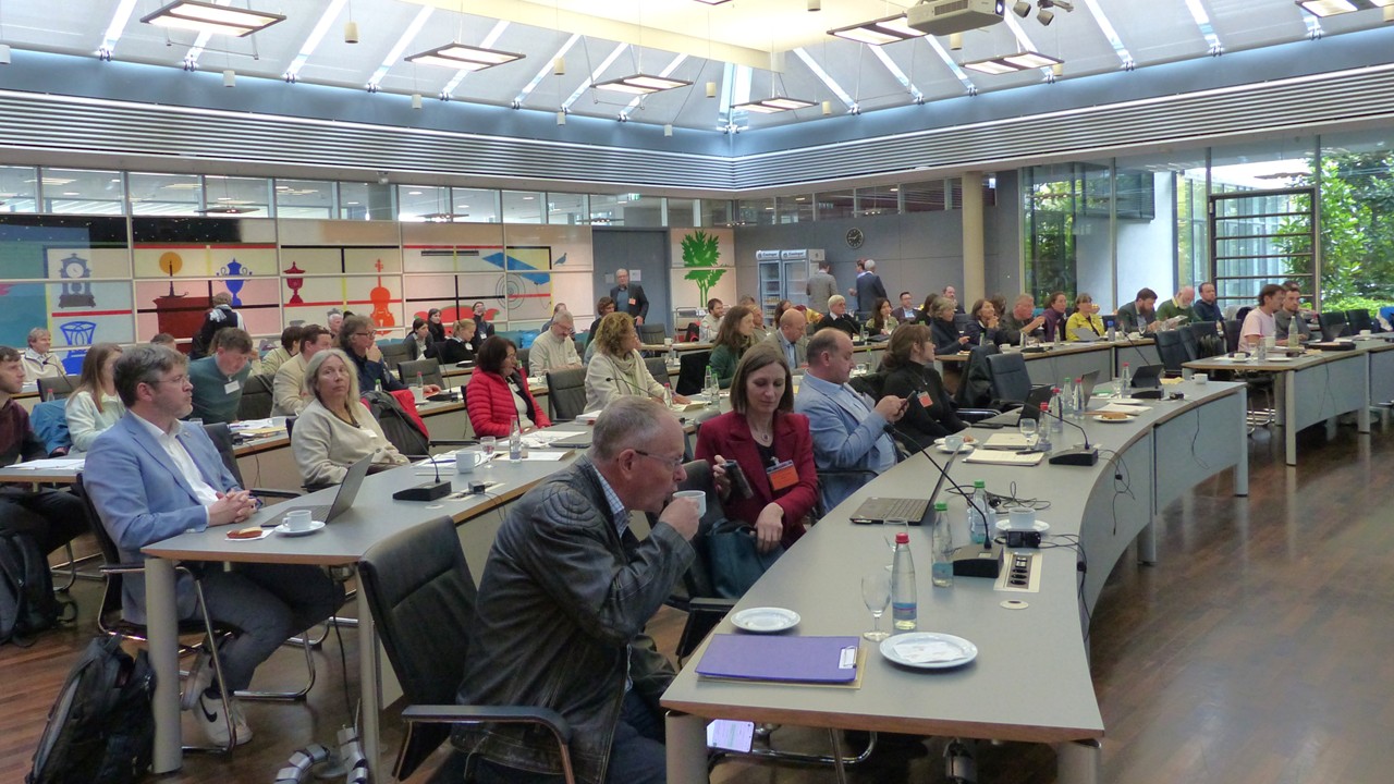 Gruppe von Leuten sitz in einem Sitzungssaal an langen Tischen